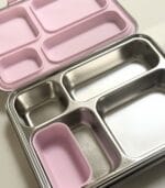 Close-up of the open Bento 4+ interior with a pink lid, showing the four stainless compartments
