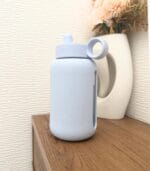 White Kaally glass water bottle standing on a wooden shelf against a textured wall