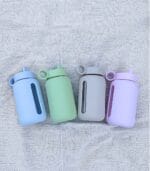 Four Kaally glass water bottles laid in a row in blue, green, grey and lilac silicone sleeves