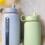 Two Kaally borosilicate glass water bottles with silicone sleeves and straw lids, styled with yellow flowers