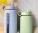 Two Kaally borosilicate glass water bottles with silicone sleeves and straw lids, styled with yellow flowers
