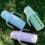 Three pastel KaakaaBaby kids glass water bottles with straw lids on grass, ready for engraved names